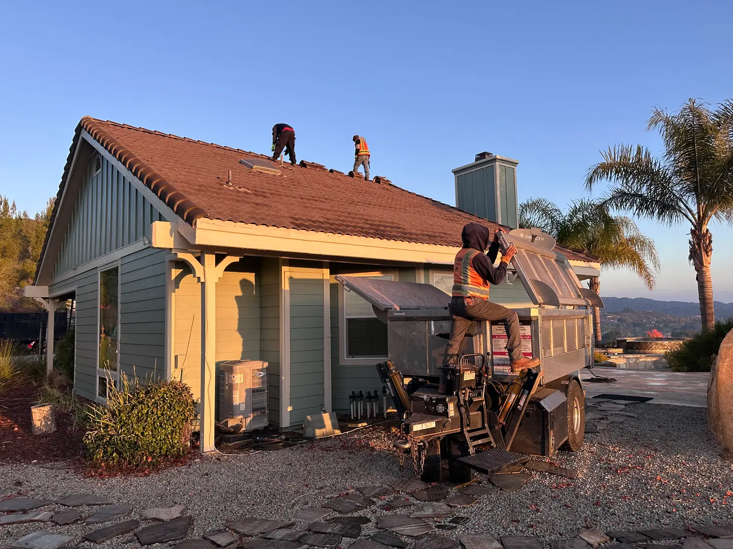 Roofers working on a tile roof with a collection truck nearby